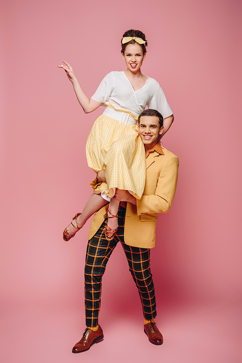 cheerful man holding happy girl while dancing boogie-woogie on pink background