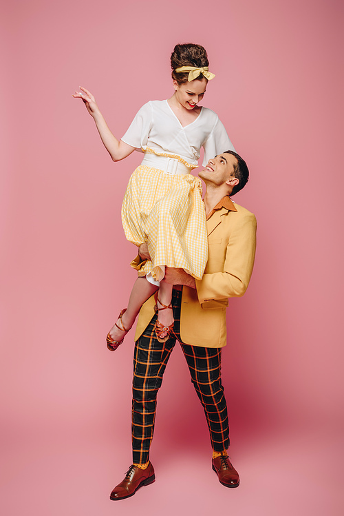 handsome man holding happy girl while dancing boogie-woogie on pink background