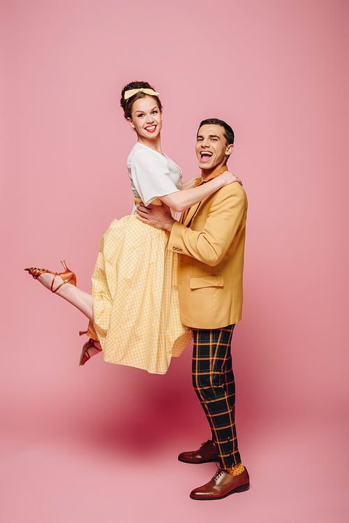 handsome man holding girl while dancing boogie-woogie on pink background