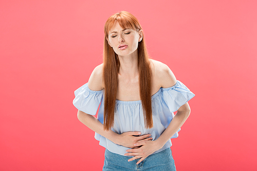 redhead woman with stomach ache touching belly with closed eyes isolated on pink