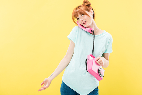 attractive redhead young woman talking on retro telephone isolated on yellow