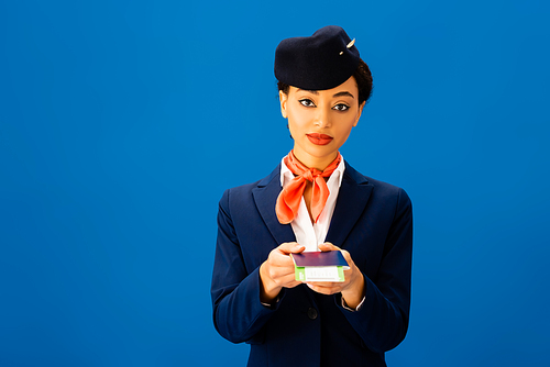 african american flight attendant holding passport and air ticket isolated on blue