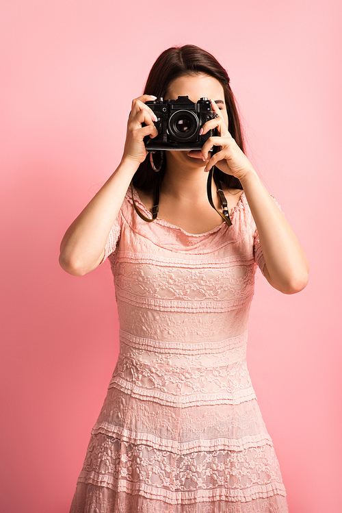 photographer in elegant dress taking photo on digital camera on pink background