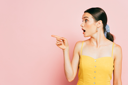 shocked brunette young woman pointing aside on pink