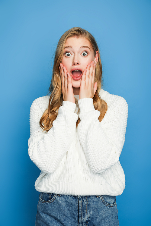 scared blonde beautiful woman in sweater isolated on blue background