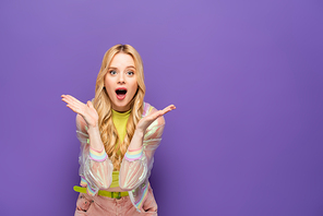 shocked blonde young woman in colorful outfit on purple background