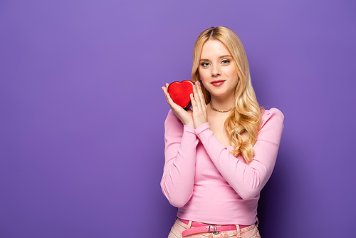 blonde young woman holding red heart shaped box on purple background