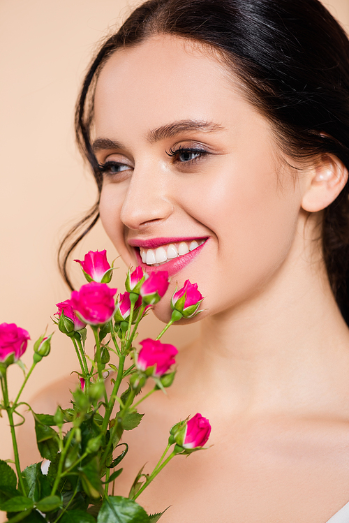 cheerful young woman smiling near flowers isolated on pink