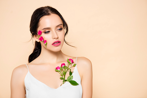 sensual young woman with flowers on face looking away isolated on pink