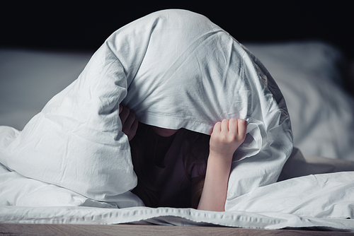 scared child hiding under blanket isolated on black