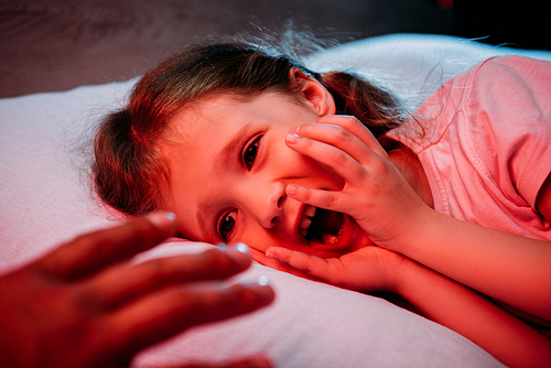 male hand near frightened, screaming child lying in bed