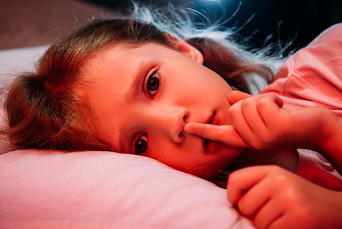 scared child lying in dark bedroom, showing hush sign and 