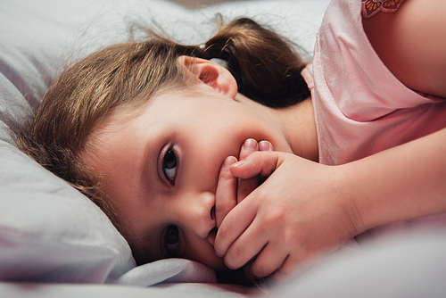 frightened kid  while lying in bed and covering mouth with hands