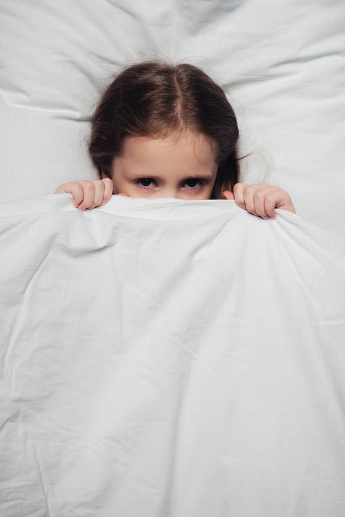 top view of scared child hiding under blanket and 