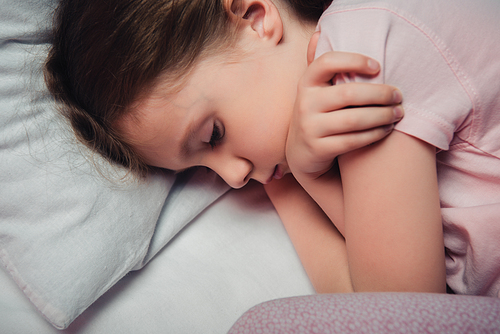 adorable frightened child lying on white bedding and embracing herself with arms