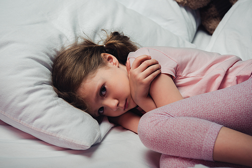 frightened child  while lying in bed and hugging herself with arms