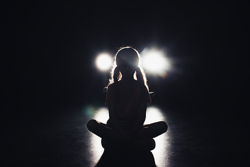 child sitting in darkness illuminated by headlights on black background