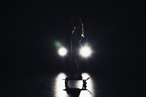 child riding penny board in darkness with illumination of headlights on black background