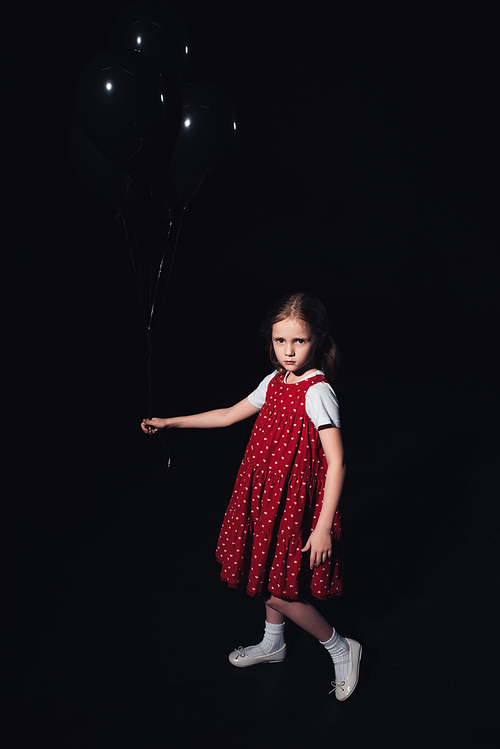 offended kid holding black balloons and  isolated on black