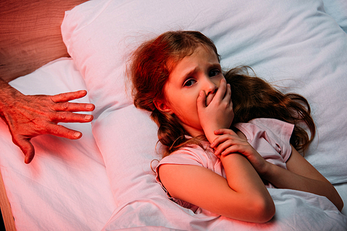 male hand near scared child showing hush sign and  while lying in bed