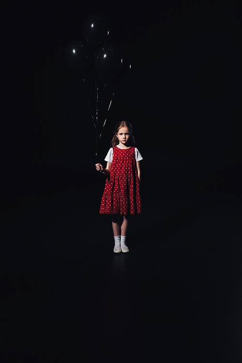 sad child standing with black balloons and  isolated on black