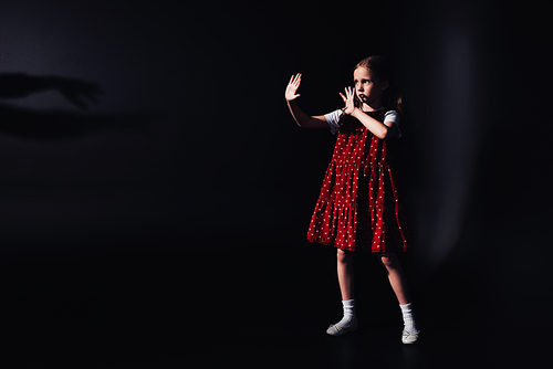 scared child standing in darkness with outstretched hands on black background