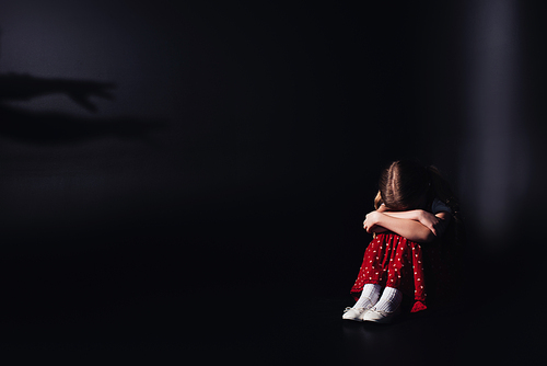 depressed, lonely child sitting with bowed head on black background