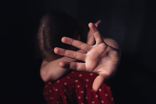selective focus of frightened, lonely child sitting with outstretched hand isolated on black