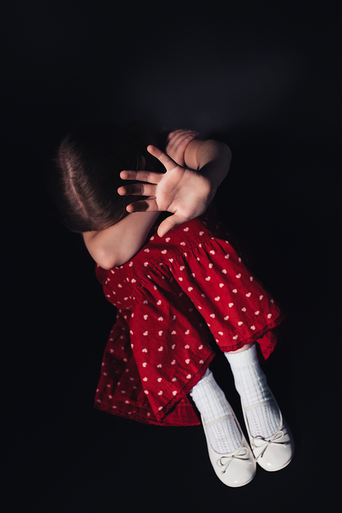 scared, lonely child sitting with outstretched hand on black background