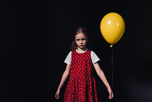 offended, lonely child with yellow balloon  isolated on black