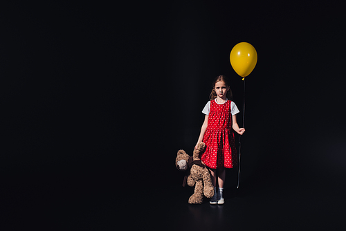 sad child with yellow balloon and teddy bear  isolated on black