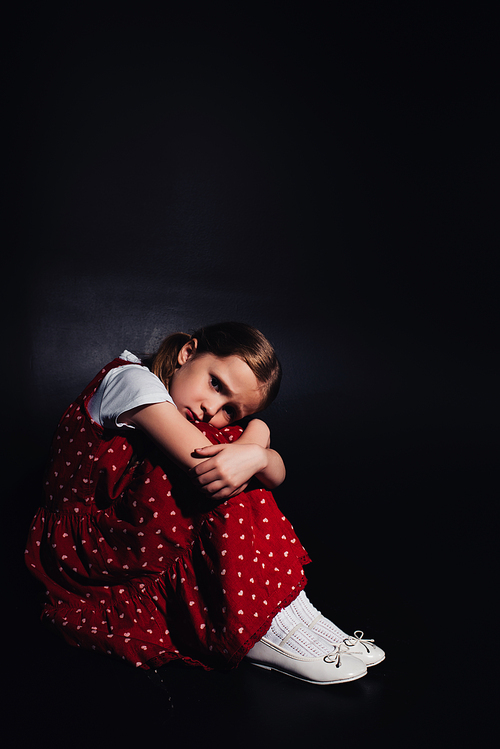 lonely, frightened child sitting on floor and  on black background