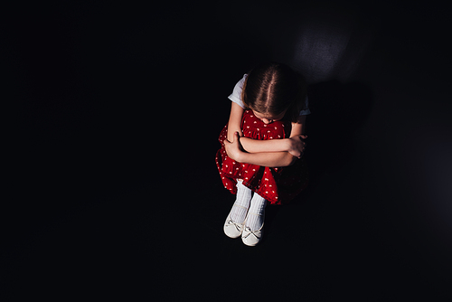 overhead view of depressed child sitting on floor on black background