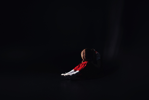 depressed, frightened kid sitting on floor with bowed head isolated on black