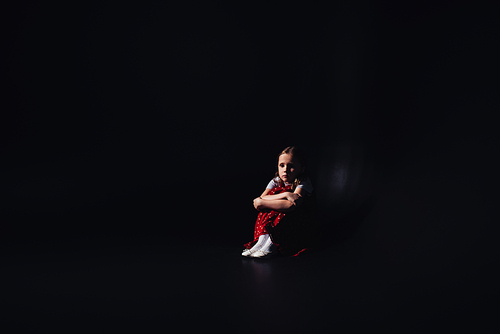 scared, lonely child sitting on floor on black background with copy space