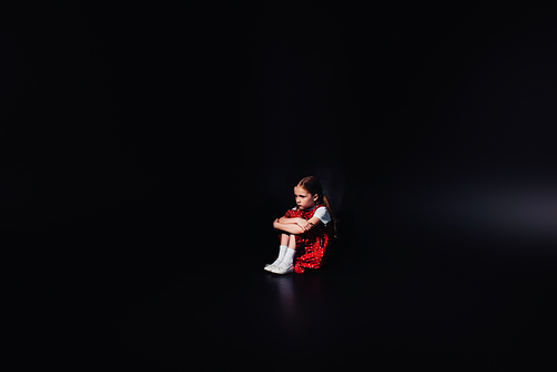 depressed, frightened kid sitting on floor isolated on black
