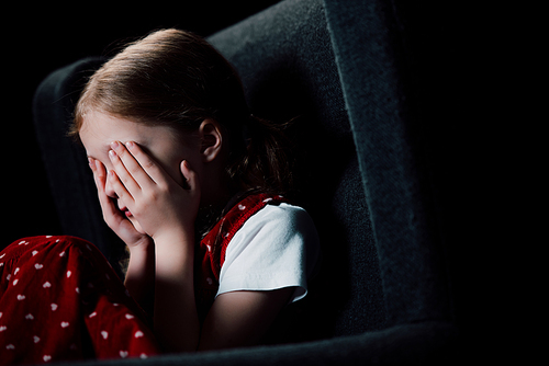 depressed, scared child covering face with hands isolated on black