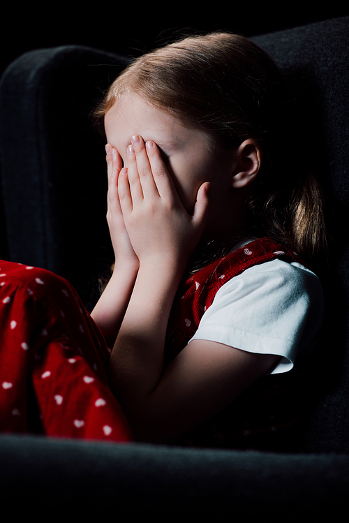 frightened child covering face with hands isolated on black