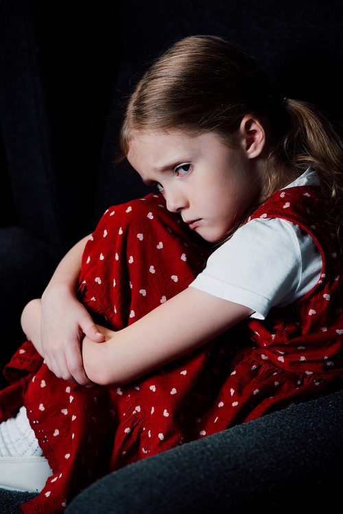 offended, frightened kid sitting in armchair isolated on black