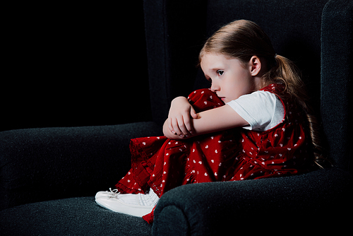 depressed, scared child sitting in armchair isolated on black