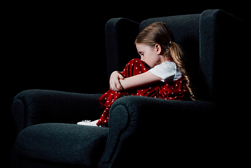 frightened, lonely child sitting in armchair isolated on black