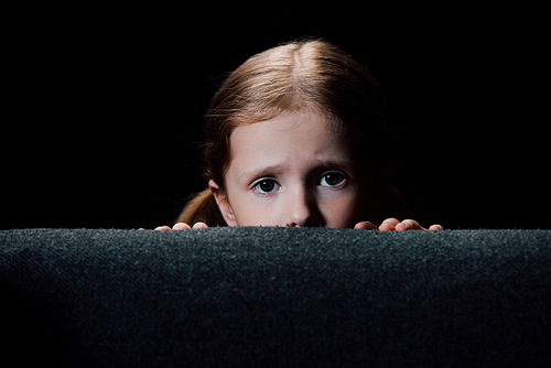 scared child hiding behind armchair and  isolated on black