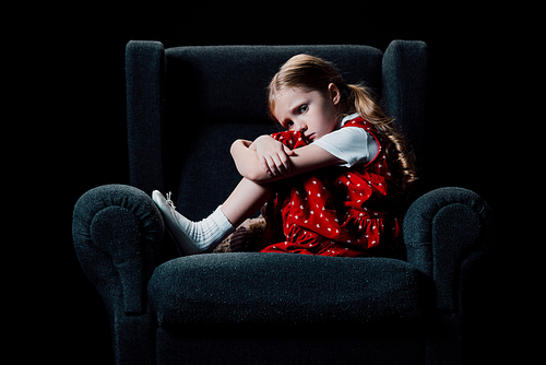 scared, lonely child sitting in armchair and  isolated on black