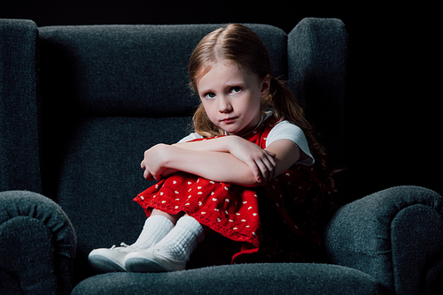 depressed, scared child sitting in armchair and  isolated on black