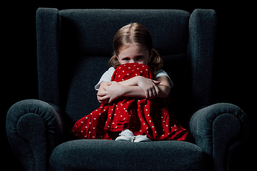 lonely, scared child sitting in armchair and  isolated on black