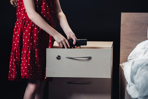 partial view of child taking gun out of nightstand isolated on black