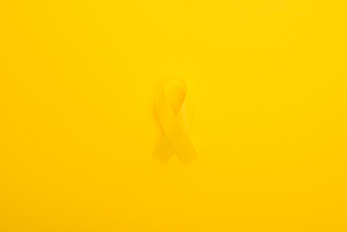 Top view of yellow ribbon on bright colorful background, international childhood cancer day concept