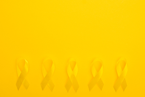 Flat lay with yellow ribbons on bright colorful background, international childhood cancer day concept