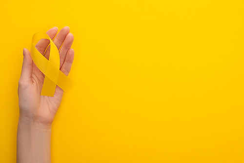 Partial view of female hand with yellow ribbon on colorful background, international childhood cancer day concept