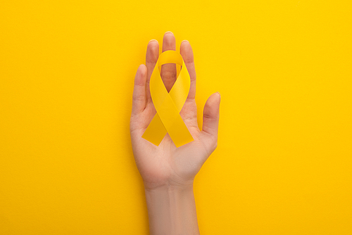 Cropped view of female hand with yellow awareness ribbon on colorful background, international childhood cancer day concept